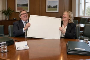 Two fictional sports directors laugh over a giant blank appointment document.