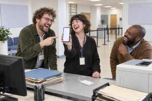 Three fictional office workers laugh as one holds a blank smartphone like an identity document.