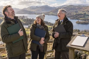 Three fictional adult National Park board administrators clearly laugh while holding blank appointment folders at a scenic overlook.