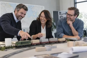 Three fictional adult rail logistics planners clearly laughing beside a freight model for rail freight growth target.