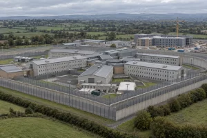 An aerial view of a modern prison complex with a new construction extension beyond its perimeter fences.