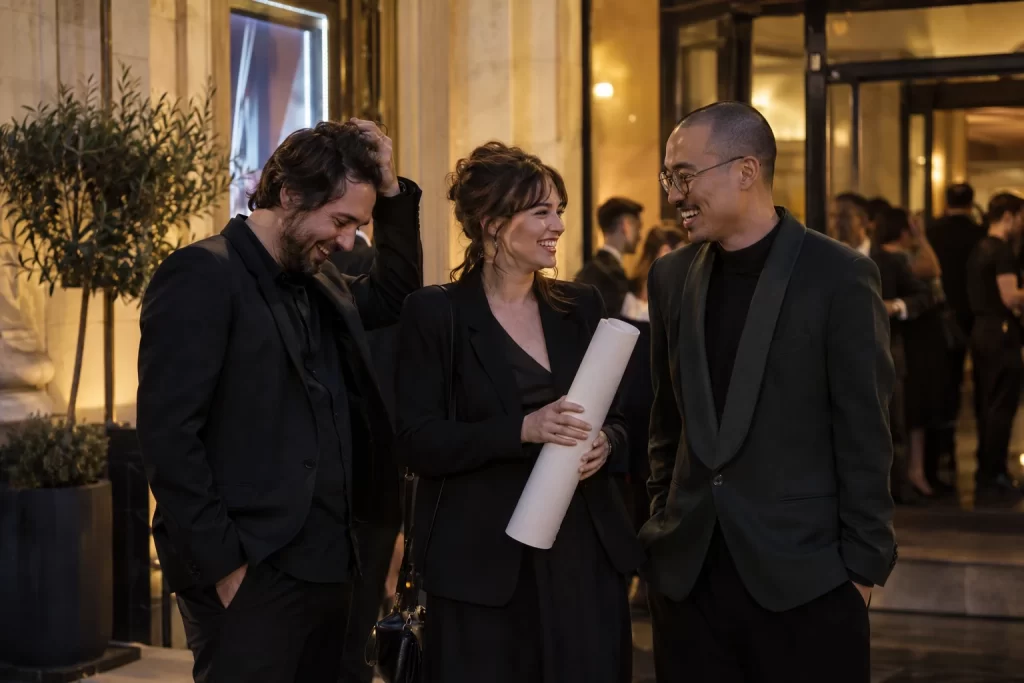Three adult independent filmmakers laugh together outside an elegant European cinema venue.