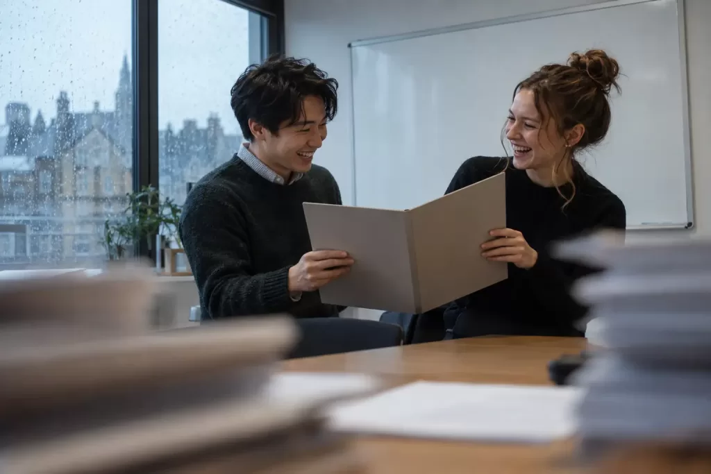 Original editorial photograph of two laughing young adults at a rainy training workshop holding a blank contract folder, with no other people