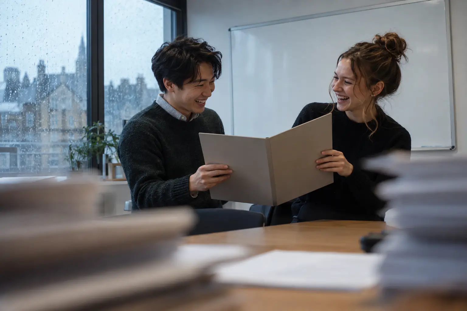 Original editorial photograph of two laughing young adults at a rainy training workshop holding a blank contract folder, with no other people