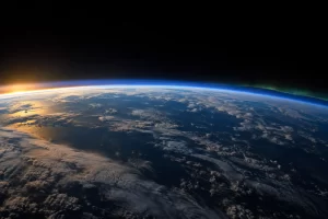 The curved blue atmospheric edge of Earth rises above clouds and ocean with a faint polar glow.