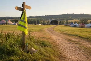 A steward vest hangs from an unmarked wayfinding post beside an empty summer festival path.