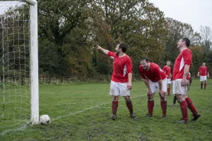 Amateur football players laughing beside a goalpost at a tree lined pitch
