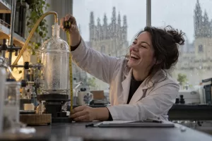 Original editorial photograph of a laughing researcher with a measuring tape beside a vacuum device for greenhouse gas removals response
