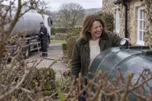 Laughing homeowner checking a heating oil tank gauge beside a laughing delivery driver at an unbranded tanker
