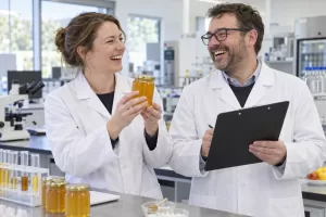 Two laughing laboratory technicians with an unlabelled honey jar for the honey authenticity testing framework