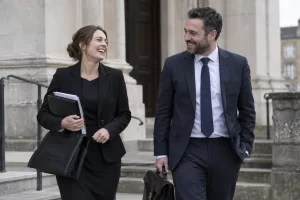 Two criminal legal aid solicitors laugh together outside a stone magistrates court with their briefcases.