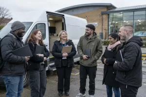 Five laughing adult jobseekers and an adviser stand beside a mobile employment-advice van.