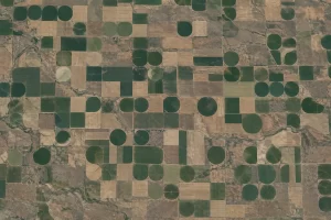 A high orbital view reveals green irrigation circles and pale rectangular fields across Montana farmland.