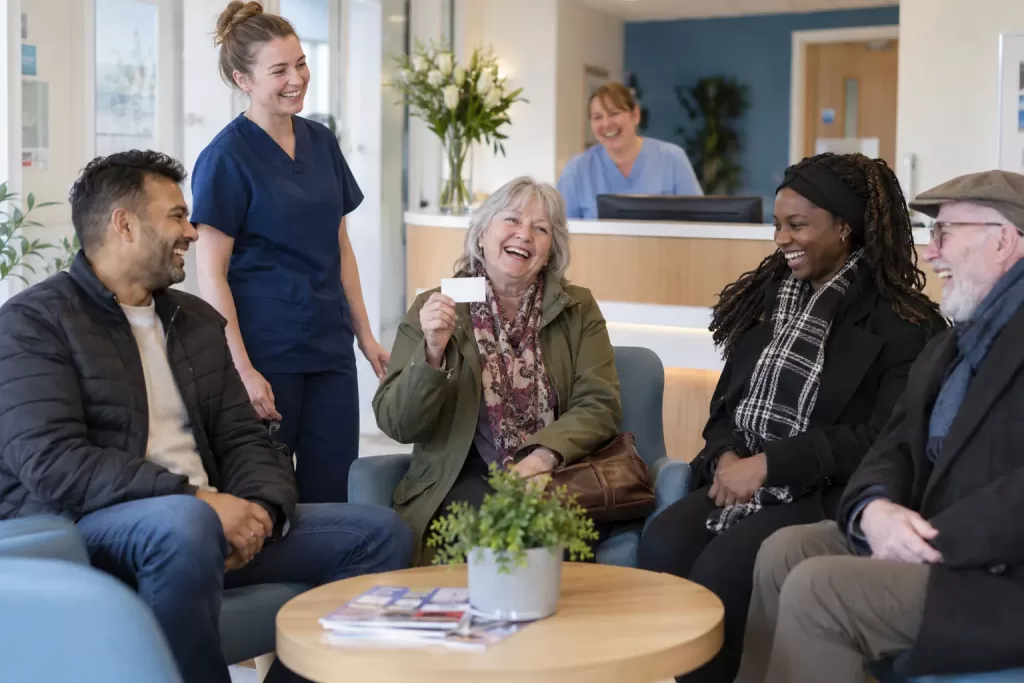 Six laughing adult patients and dental staff in a bright NHS-style dental waiting room.
