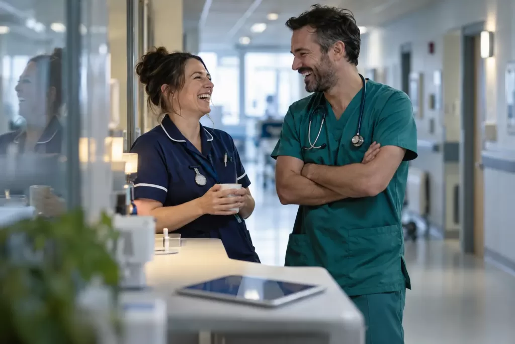 Two laughing clinicians in a fictional NHS single patient record 2026 corridor scene