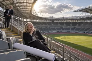 Two laughing planners at fictional North of England Olympics assessment 2026 stadium