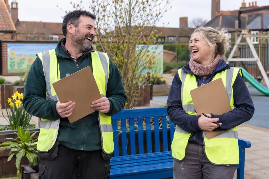 Two laughing community volunteers beside a bench representing the Pride in Place programme