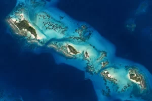 A high orbital view shows sandy tropical islands and reef channels in clear blue ocean.