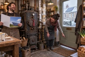 Two fictional adults laugh beside an ancient boiler in a small shop while pointing out a draught under the door, with insulation and a solar panel visible.