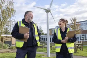 Two laughing facilities workers by a small wind turbine representing small onshore wind turbines