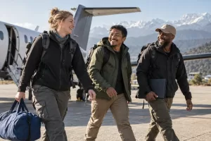 Original editorial photograph of three laughing emergency-response workers with a plain blue duffel beside an unmarked small aircraft and Himalayan foothills, with no text or logos