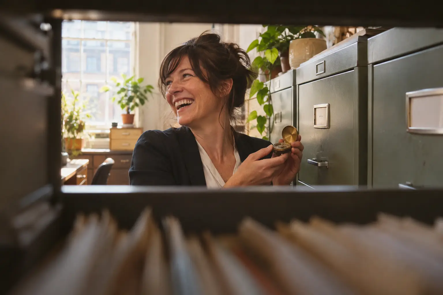 Original editorial photograph of a laughing woman with a compass beside a filing cabinet for women criminal justice policy