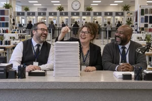Zero Waste Day repair officials clearly laughing over paperwork for one shirt button at a fictional national service counter.